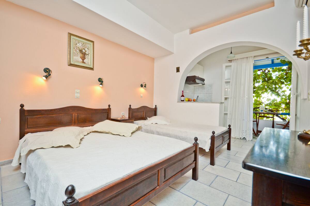 A bedroom with two beds, a wooden headboard, a nightstand, a small table, and a view of the outdoors through an archway.