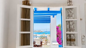 A room with a window, a small table with a lamp, and a view of a coastal area. - Sea View Apartments & Studios (Naxos)