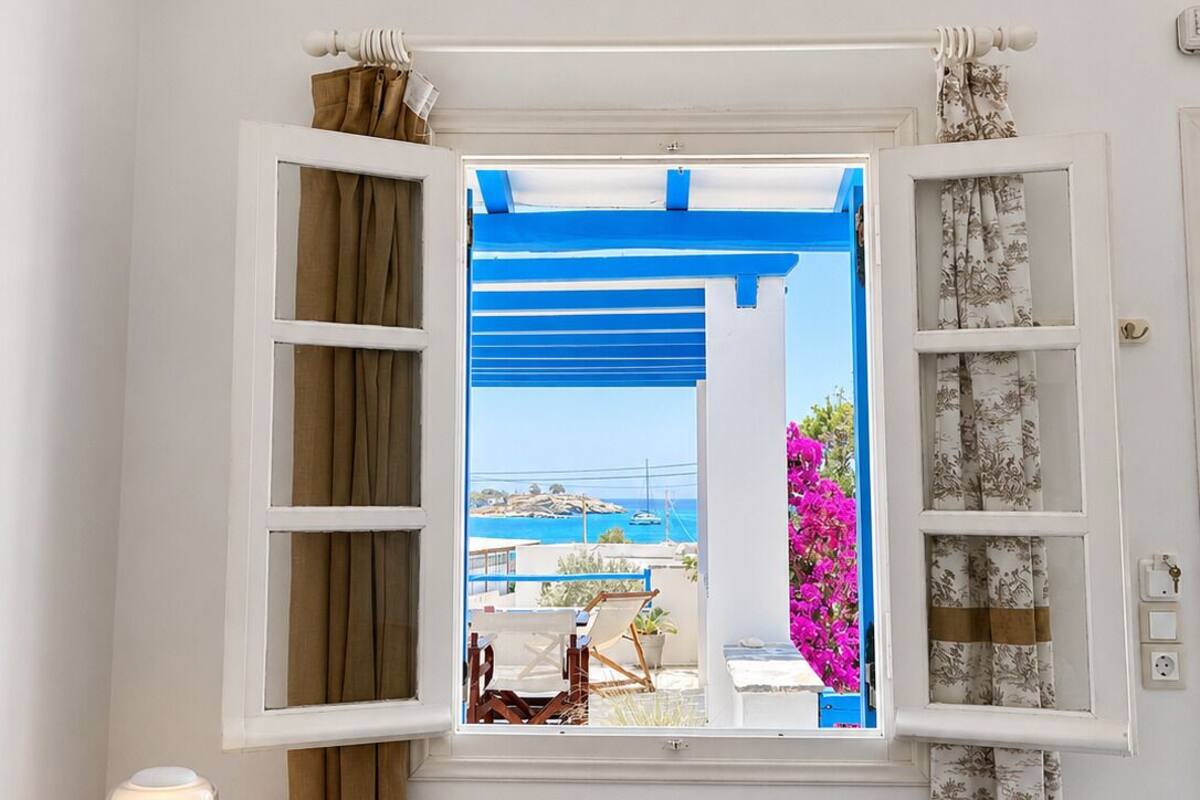 A room with a window, a small table with a lamp, and a view of a coastal area.