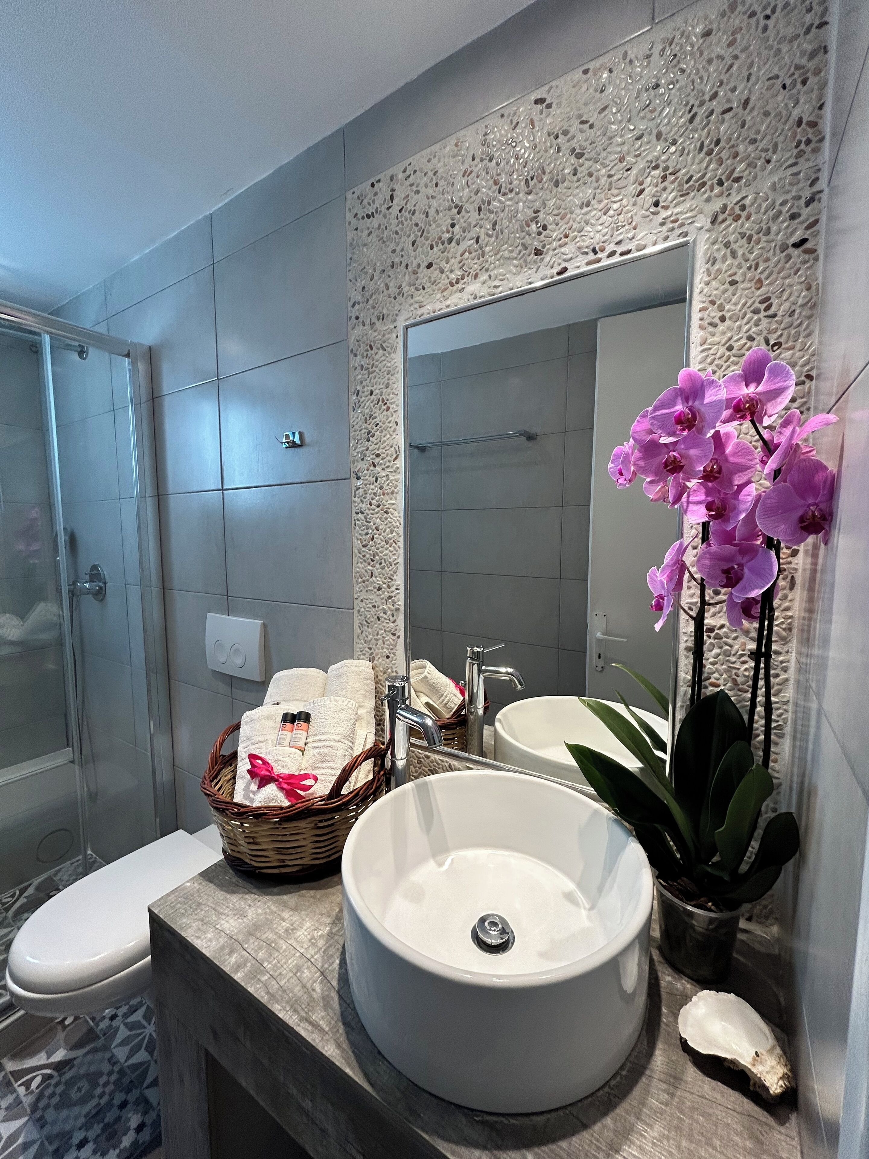 Une salle de bain moderne avec un grand miroir, deux lavabos, une douche et une plante décorative, une orchidée.
