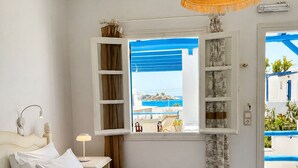 A bedroom with a bed, a window with a view, a hanging light fixture, and a bedside table. - Sea View Apartments & Studios (Naxos)