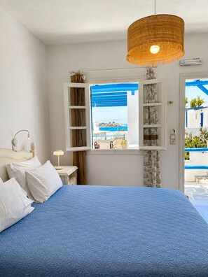 A bedroom with a bed, a window with a view, a hanging light fixture, and a bedside table. - Sea View Apartments & Studios (Naxos)