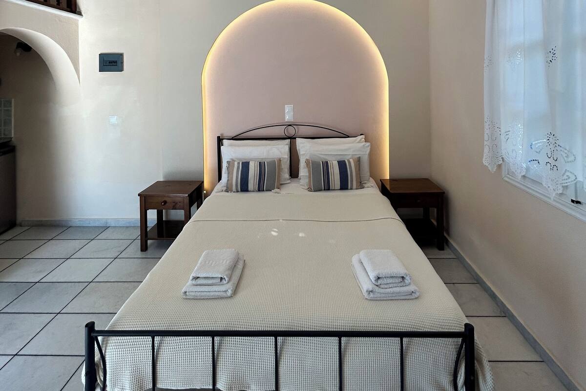 A bedroom with a bed, nightstands, a small table, and a window with curtains.