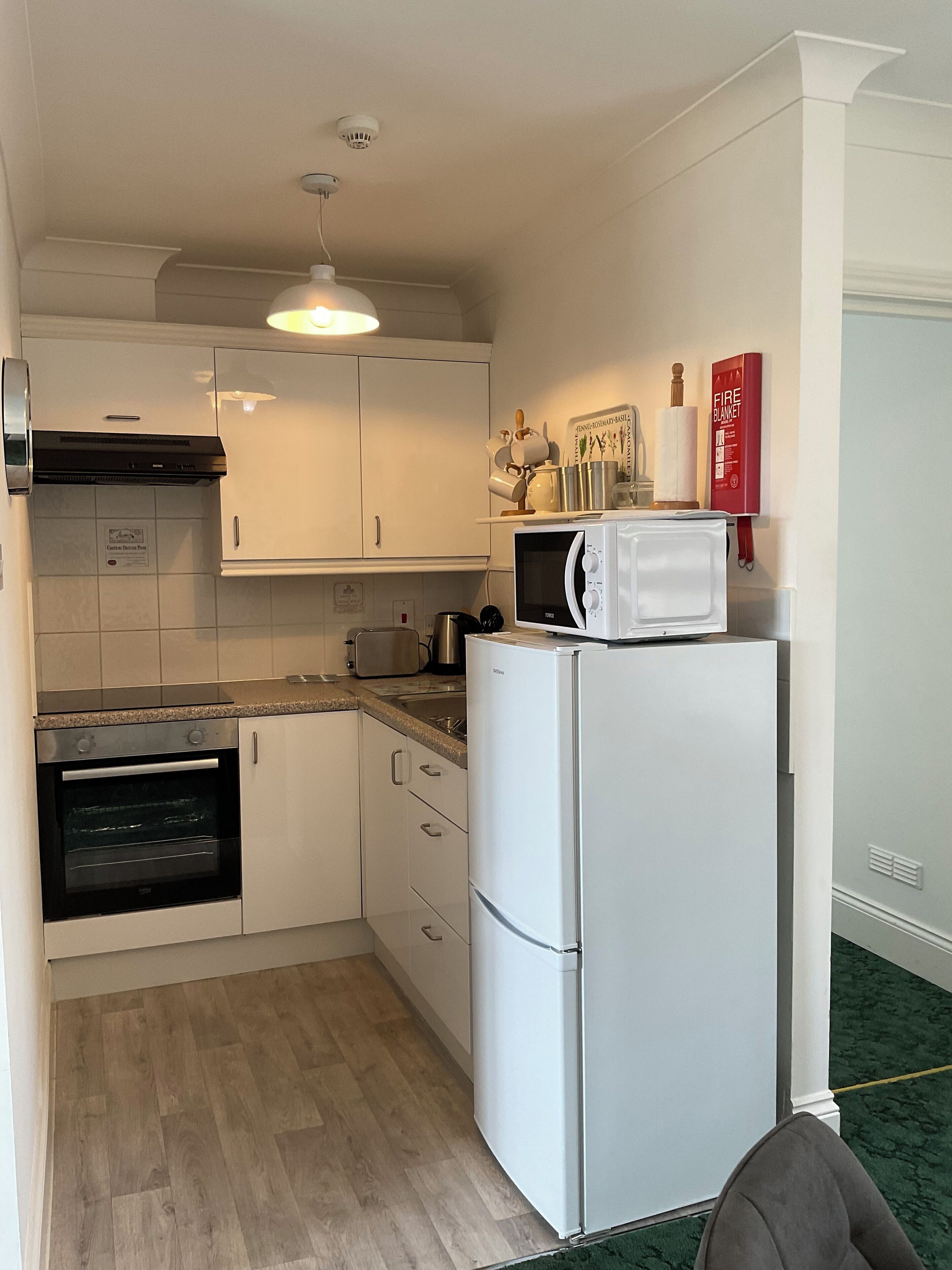 A compact kitchen with white cabinets, a microwave, a toaster, and a refrigerator.