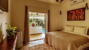 Un dormitorio con una cama, una mesita de noche de madera, una planta en maceta y vistas al exterior.