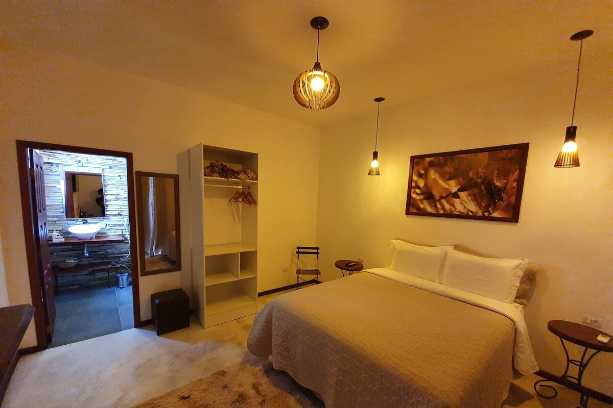 A bedroom with a bed, a wardrobe, a mirror, a painting, and a small table.