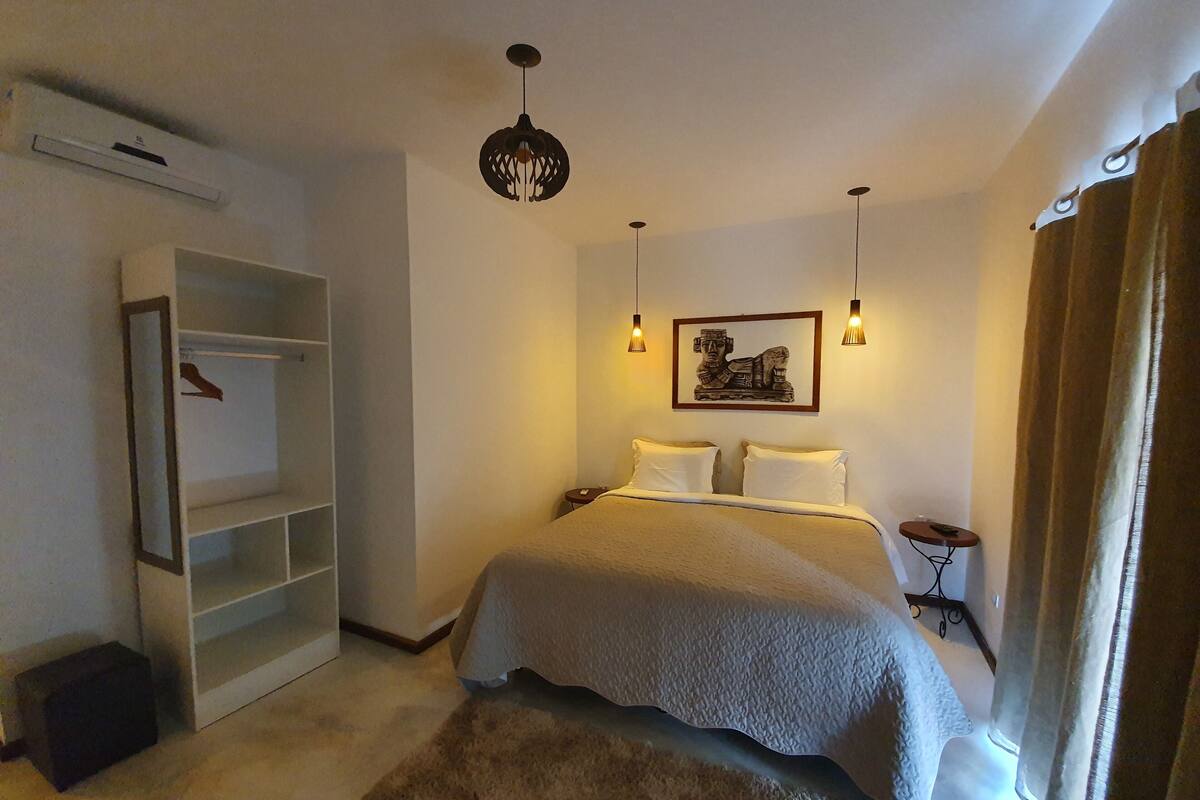 A bedroom with a bed, a hanging light fixture, a wall-mounted picture, and a wardrobe.