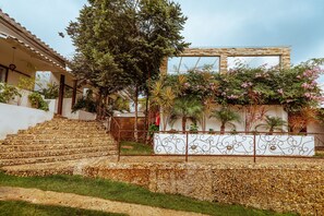 Una escalera de piedra que sube hacia un edificio con pared blanca y una cerca metálica.