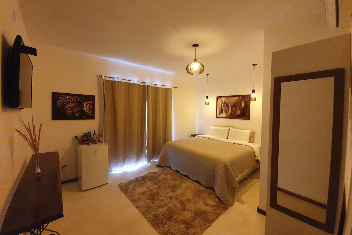A bedroom with a bed, a desk, a chair, a wardrobe, and a painting on the wall.