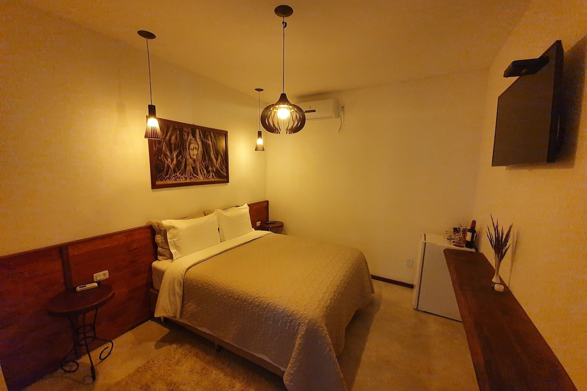 A bedroom with a bed, bedside table, lamp, and a painting on the wall.