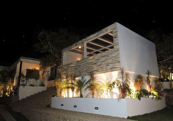 A modern house with a stone facade, large windows, and a well-lit entrance. - Pousada Casa de Shiva (Alto Paraíso de Goiás)