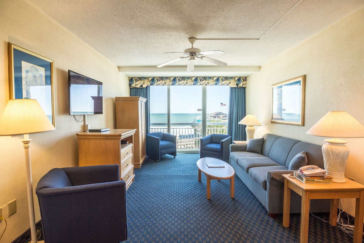 A hotel room with a balcony, a TV, a desk, and a sofa.
