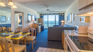 A hotel room with a dining area, a living area, a kitchenette, and a balcony with a view.