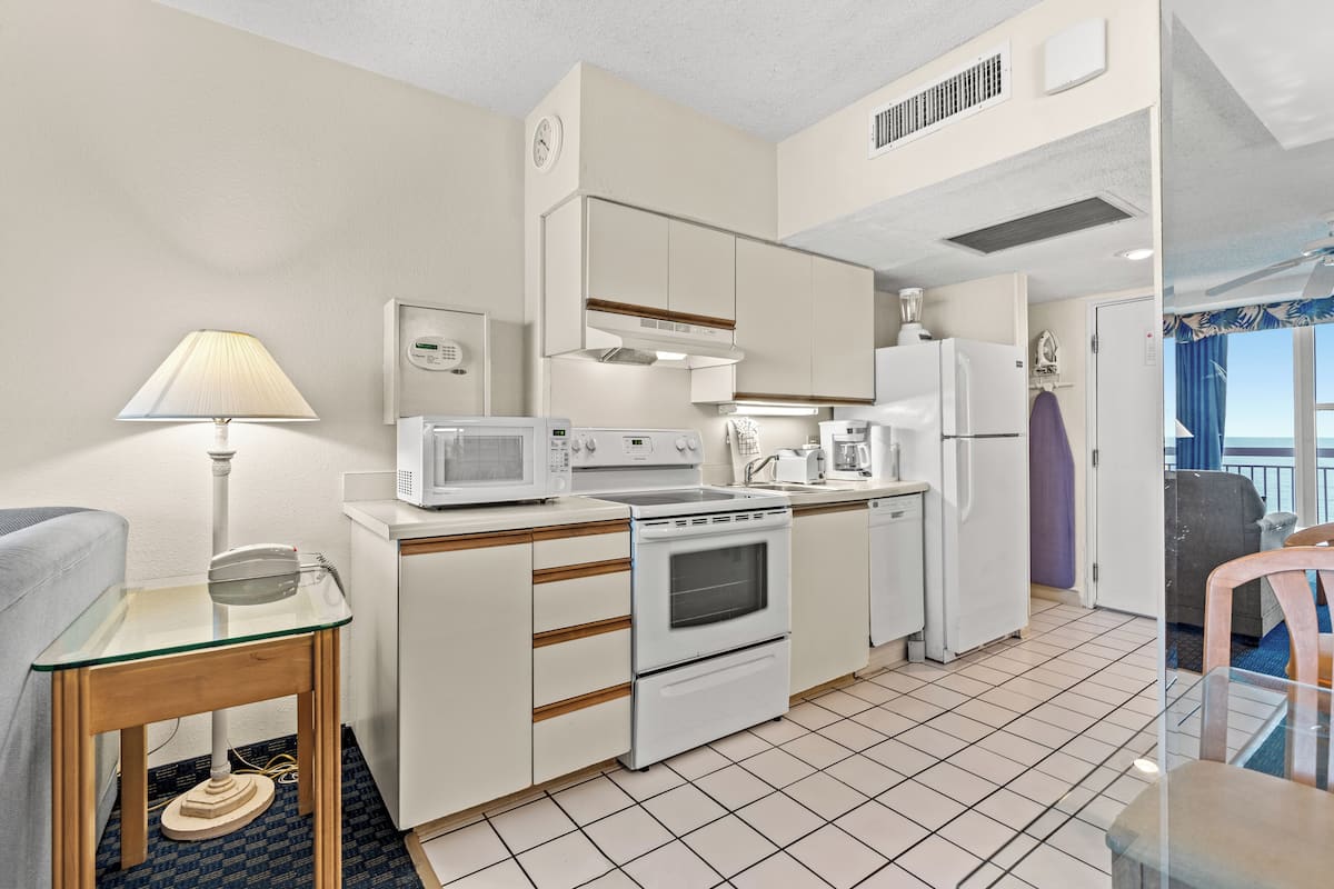 A compact kitchen with white appliances, a glass table, and a view of the outside.