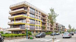 A multi-story residential building with balconies, a parking area, and a street view. - La Bohème 204 (Koksijde)