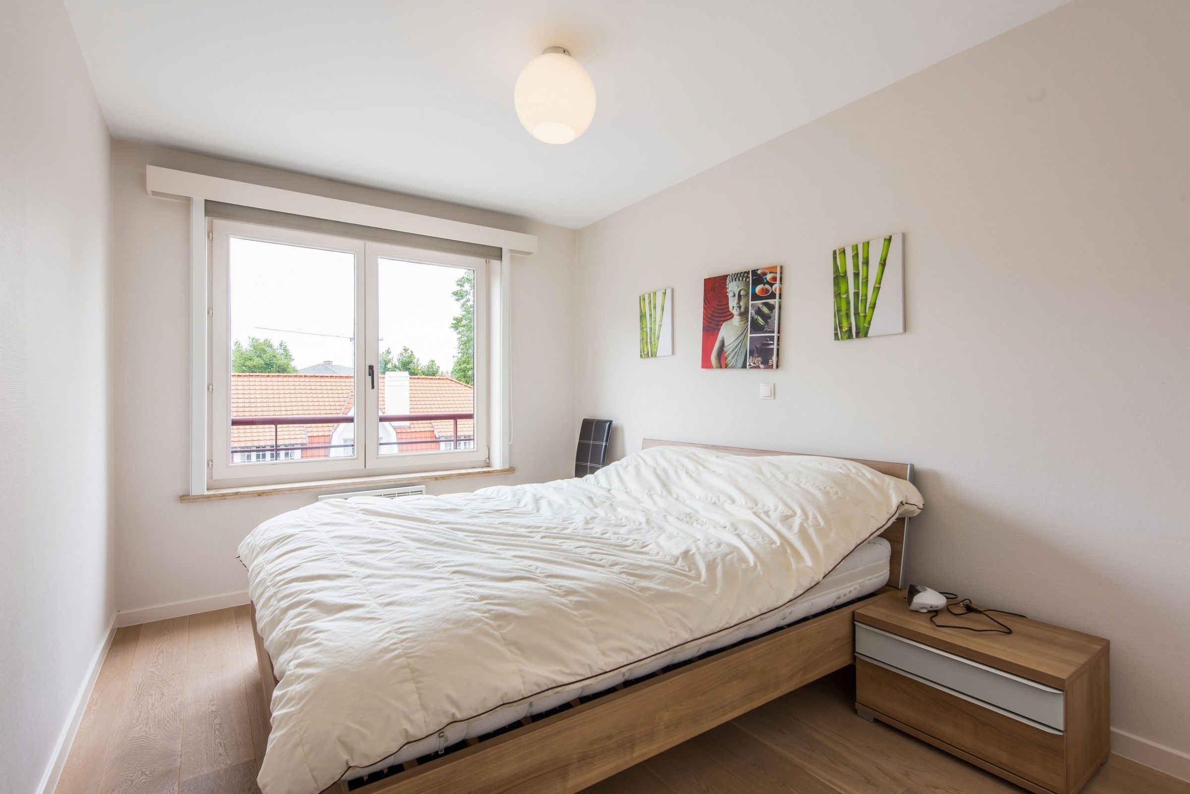 A bedroom with a bed, a nightstand, a window, and wall art.