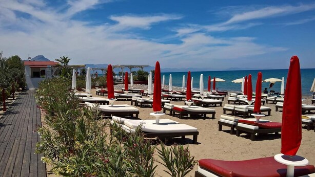 A beachside hotel with rows of sun loungers and umbrellas, a wooden walkway, and a view of the sea and mountains. - B&B Il Muretto (Lascari)