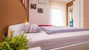 A bedroom with a bed, a bedside table, a potted plant, and a window with curtains. - B&B Il Muretto (Lascari)