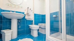 A bathroom with a sink, bidet, and toilet, all in white, against blue tiled walls. - B&B Il Muretto (Lascari)