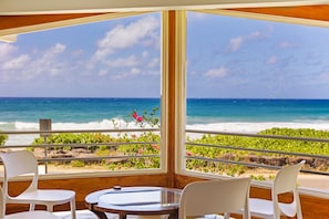 A room with a large window overlooking a beach, two white chairs, and a small table.