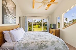 A bedroom with a bed, a ceiling fan, a television, and a view of a golf course.