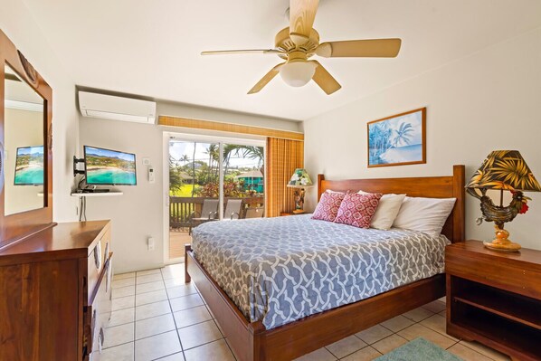 A bedroom with a bed, a ceiling fan, a TV, and a balcony with a view of the outdoors.