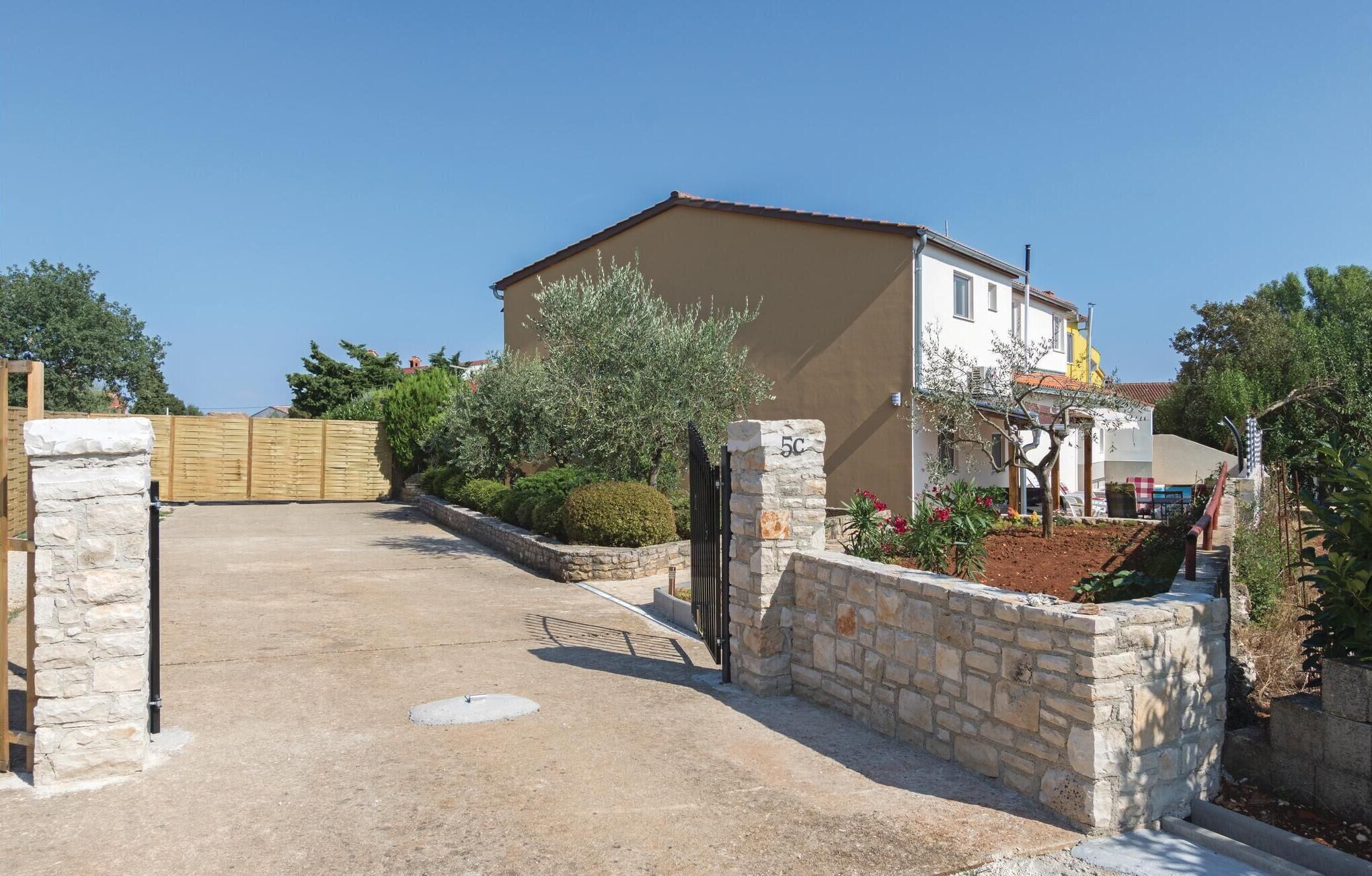 A two-story house with a stone entrance, a paved driveway, and a garden with various plants and flowers.
