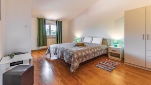 Een slaapkamer met een bed, nachtkastjes, een kledingkast, een raam met gordijnen en een tafeltje met een plant.
