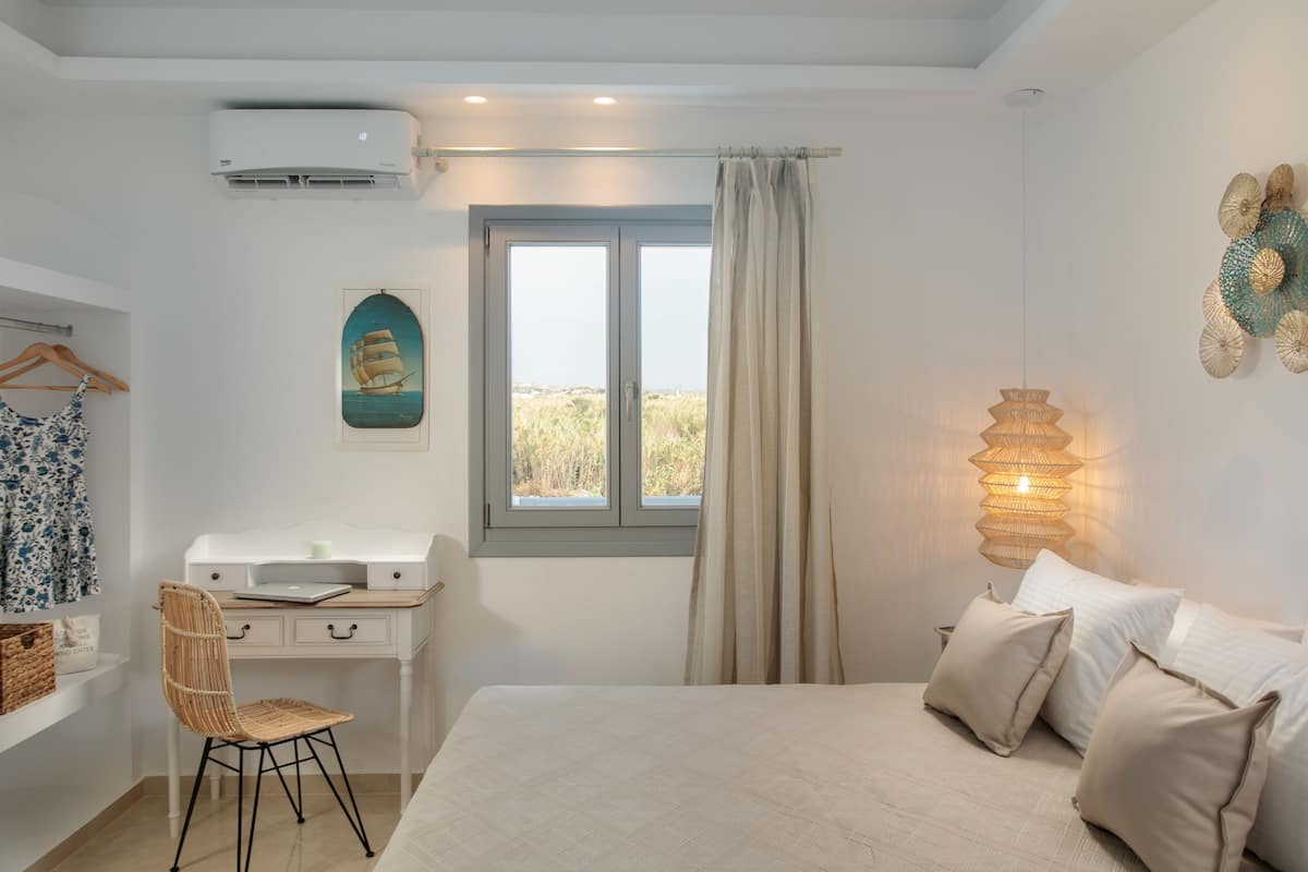 A bedroom with a bed, a desk, a chair, a window with curtains, and a wall-mounted light fixture.