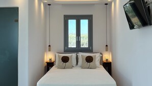 Un dormitorio con cama, mesitas de noche, una ventana y un televisor montado en la pared.