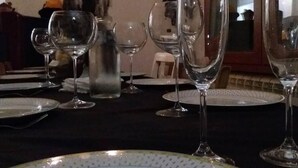 Een eettafel gedekt met meerdere wijnglazen en borden, een kandelaar met brandende kaarsen, en een rustieke wanddecoratie.