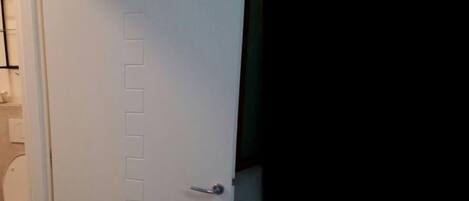 A white door with a silver handle and a keyhole, leading to a bathroom with a toilet and a shower area.
