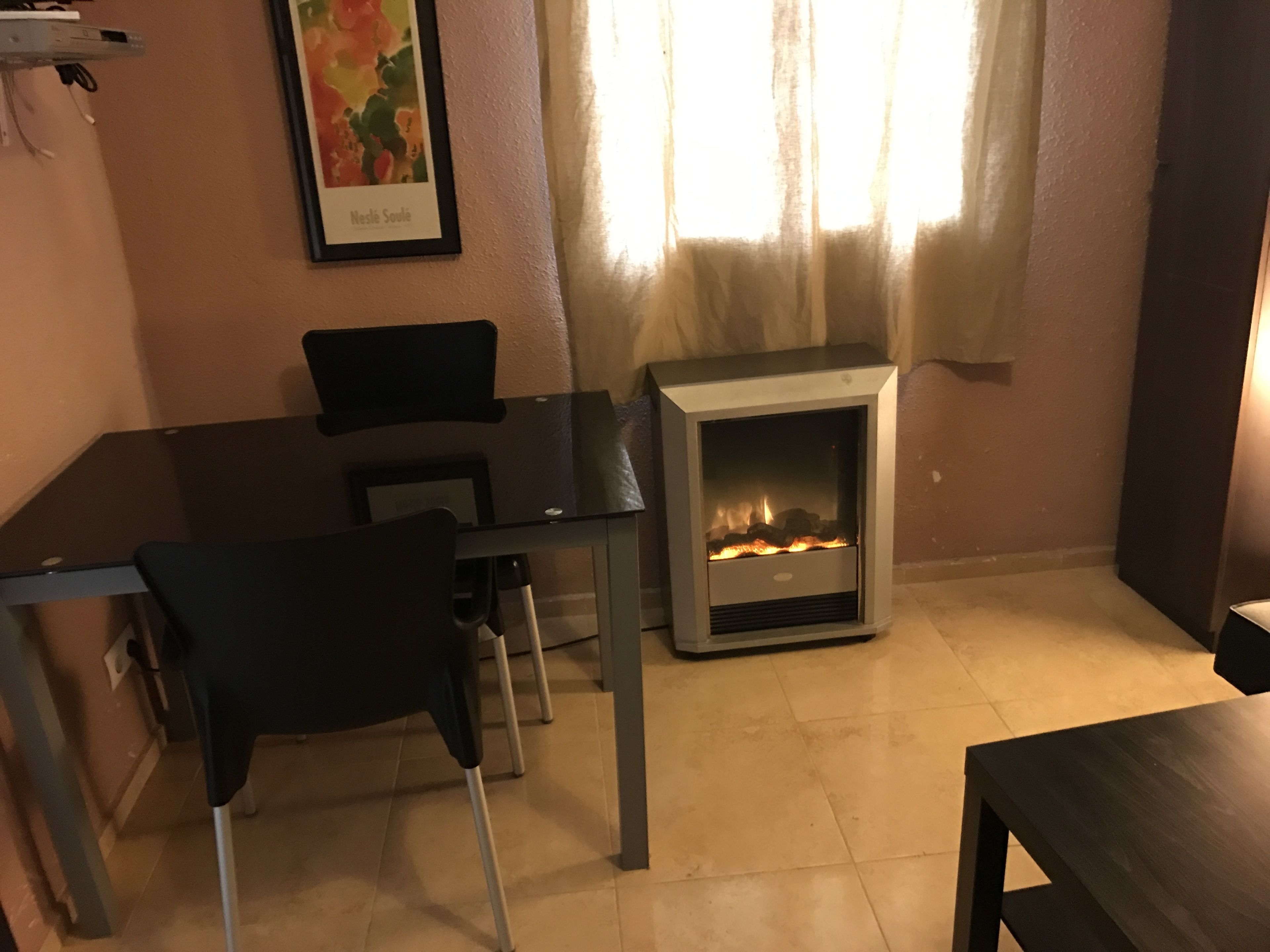 Een kamer met een open haard, een eettafel met stoelen en een ingelijst schilderij aan de muur.