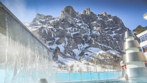 A hot spring with a waterfall feature, a mountain backdrop, and a modern structure with a conical roof. - B&B La Forge de Diogne (Crans-Montana)