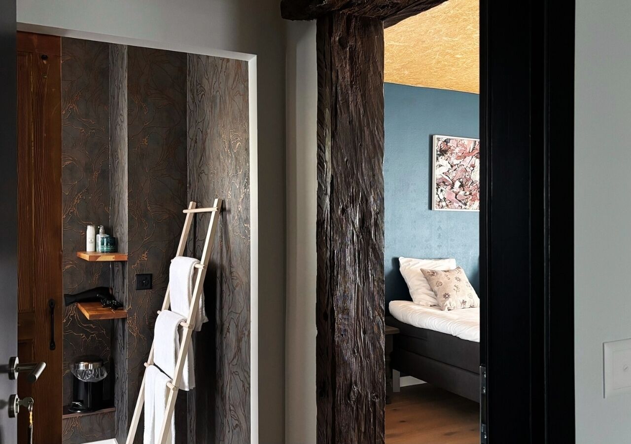 A room with a wooden ladder, a bed, a blue wall, and a shelf with toiletries.