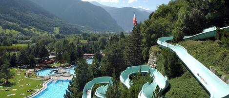 Un parque acuático con toboganes y una piscina rodeada de abundante vegetación y montañas.