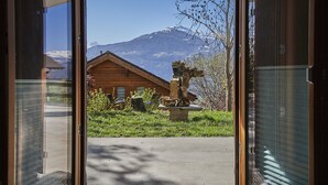 A wooden cabin with a stone sculpture in the yard, a mountain in the background, and a clear sky. - B&B La Forge de Diogne (Crans-Montana)