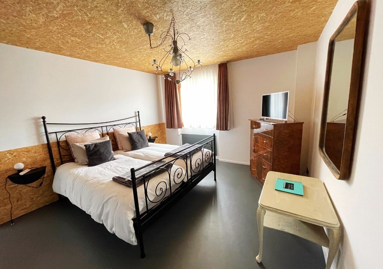 A bedroom with a bed, a desk, a dresser, a TV, and a mirror.