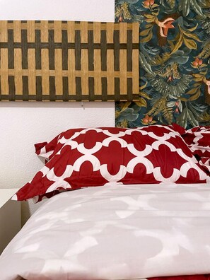 Ein Bett mit roten und weißen Kissen und einem gemusterten Bezug, ein Holz-Kopfteil und blumiger Wandteppich.