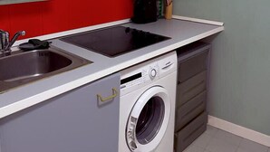 A compact kitchen with grey cabinets, a red backsplash, a built-in stove, a sink, and a front-loading washing machine. - Sol Carlos V Apartaments & Suites (Madrid)