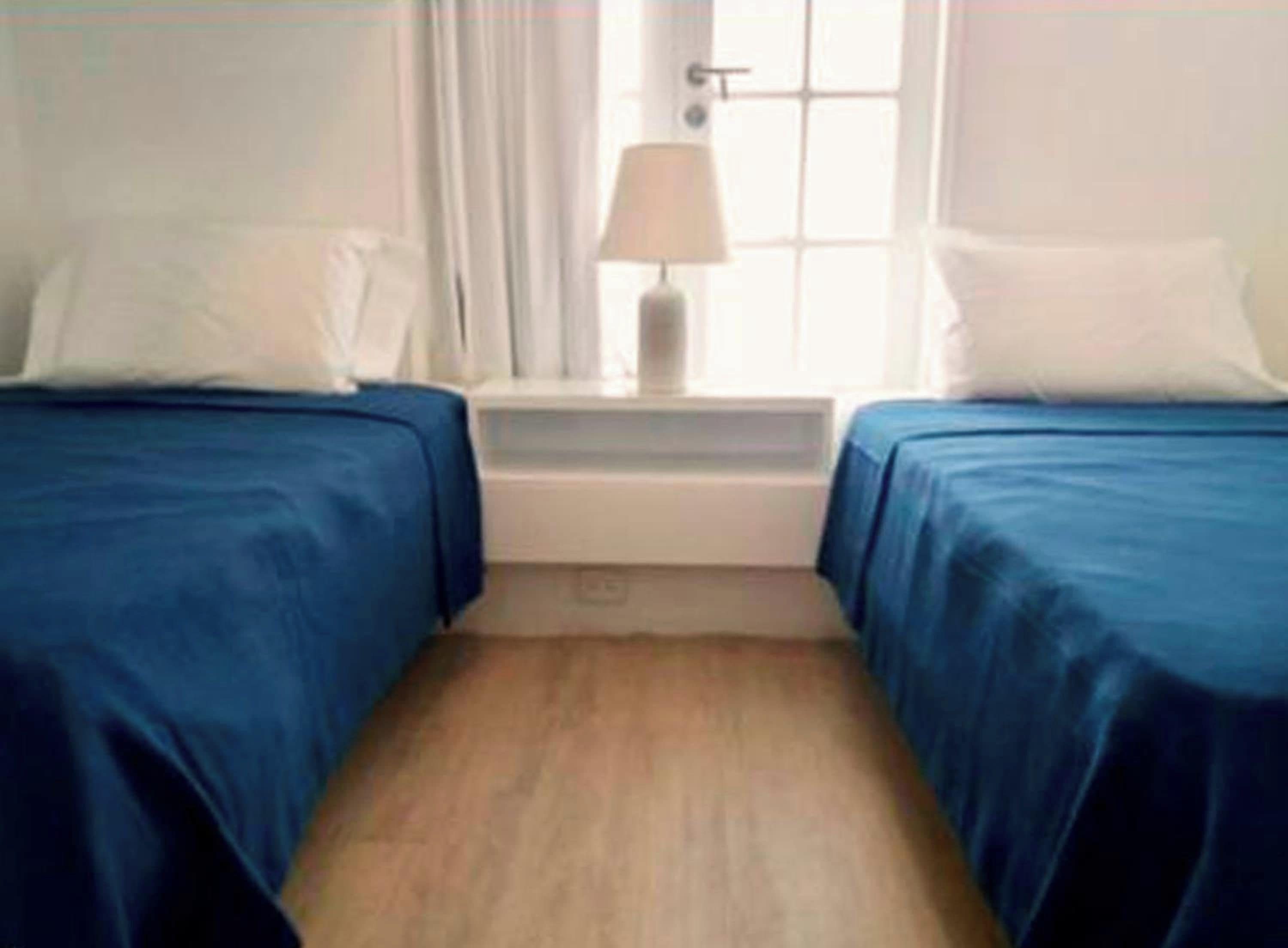 A room with two beds, a nightstand, a lamp, and a window.