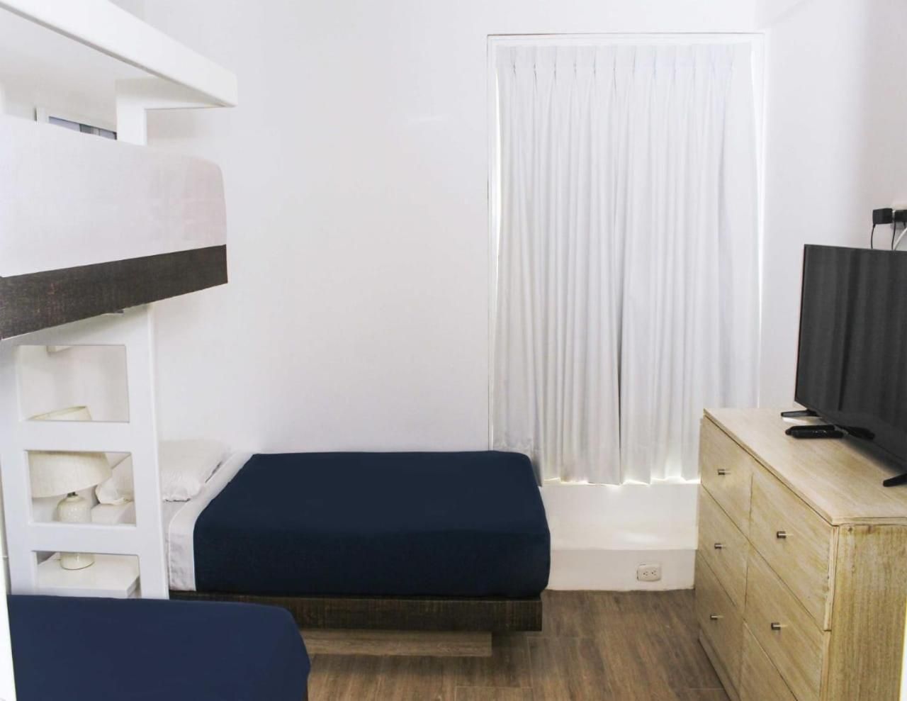 Habitación pequeña con una litera, una cama individual, un televisor sobre un tocador y una ventana con cortinas.