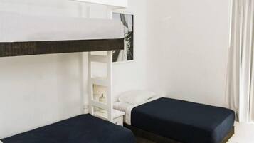 Una habitación con dos camas individuales, una mesita de noche blanca, un estante blanco y una ventana con cortinas.