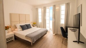 Una habitación de hotel moderna con una cama grande, un escritorio con televisión de pantalla plana y vistas al mar a través de las ventanas.