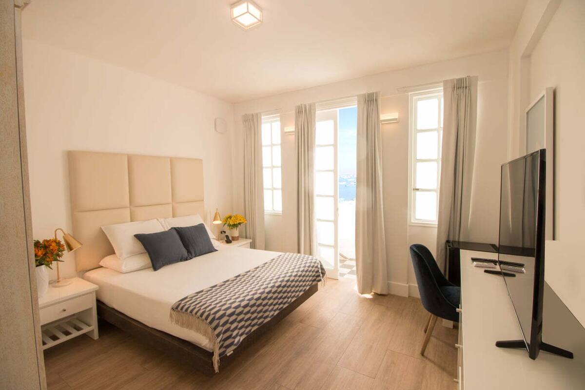Ein modernes Hotelzimmer mit einem großen Bett, einem Schreibtisch mit Flachbildfernseher und Meerblick durch die Fenster.