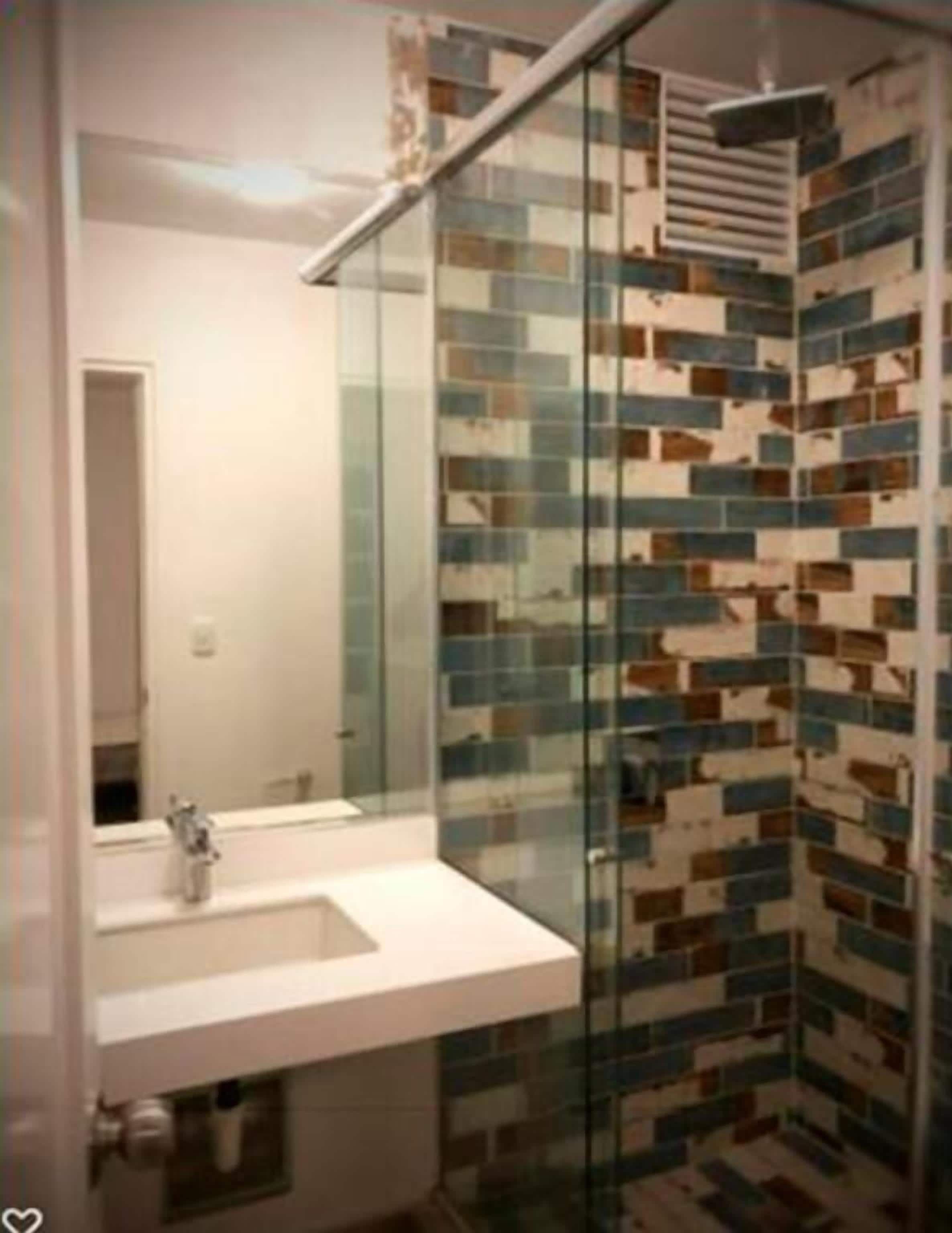 A bathroom with a glass shower enclosure, a white sink, and a tiled wall with a geometric pattern.