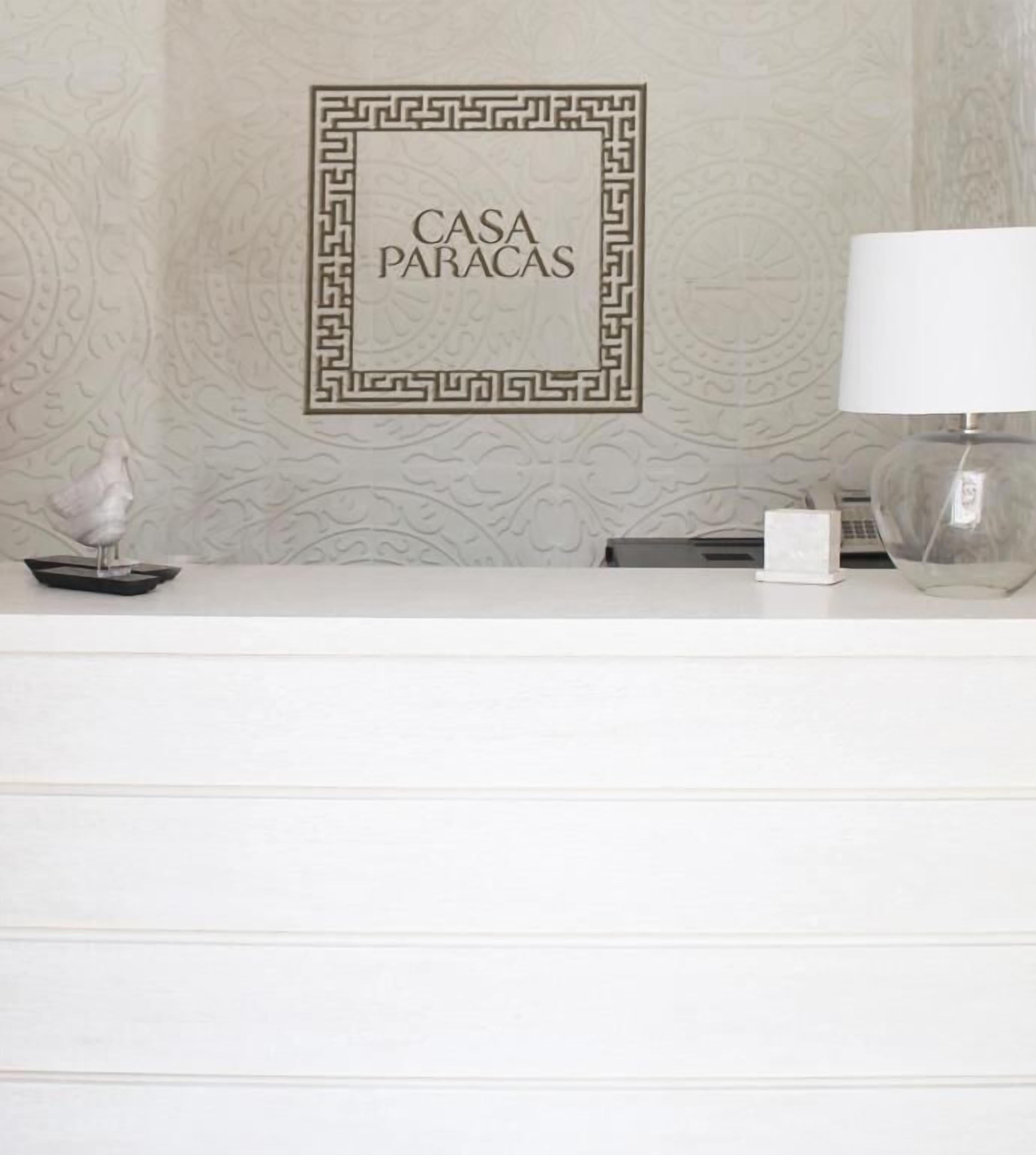 A reception desk with a framed sign reading "CASA PARACAS" and a decorative lamp.