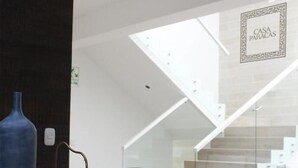 Un interior moderno con una escalera de cristal, un jarrón azul y ollas de cobre sobre una mesa blanca.