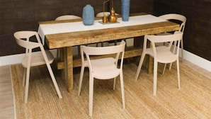 Un comedor con una mesa de madera, sillas blancas y un tapete tejido.