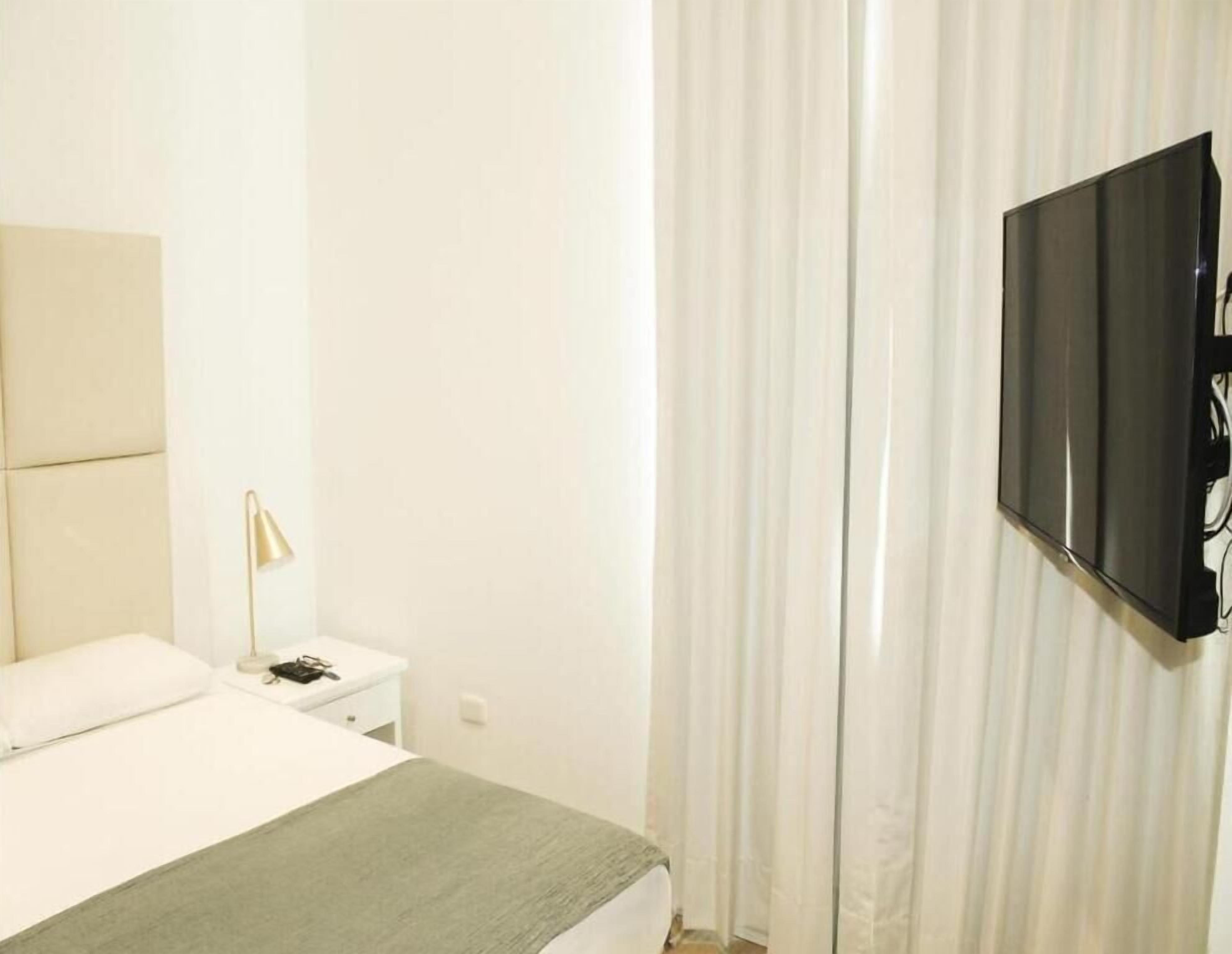 Una habitación de hotel con una cama, una mesita de noche, una lámpara y un televisor montado en la pared.